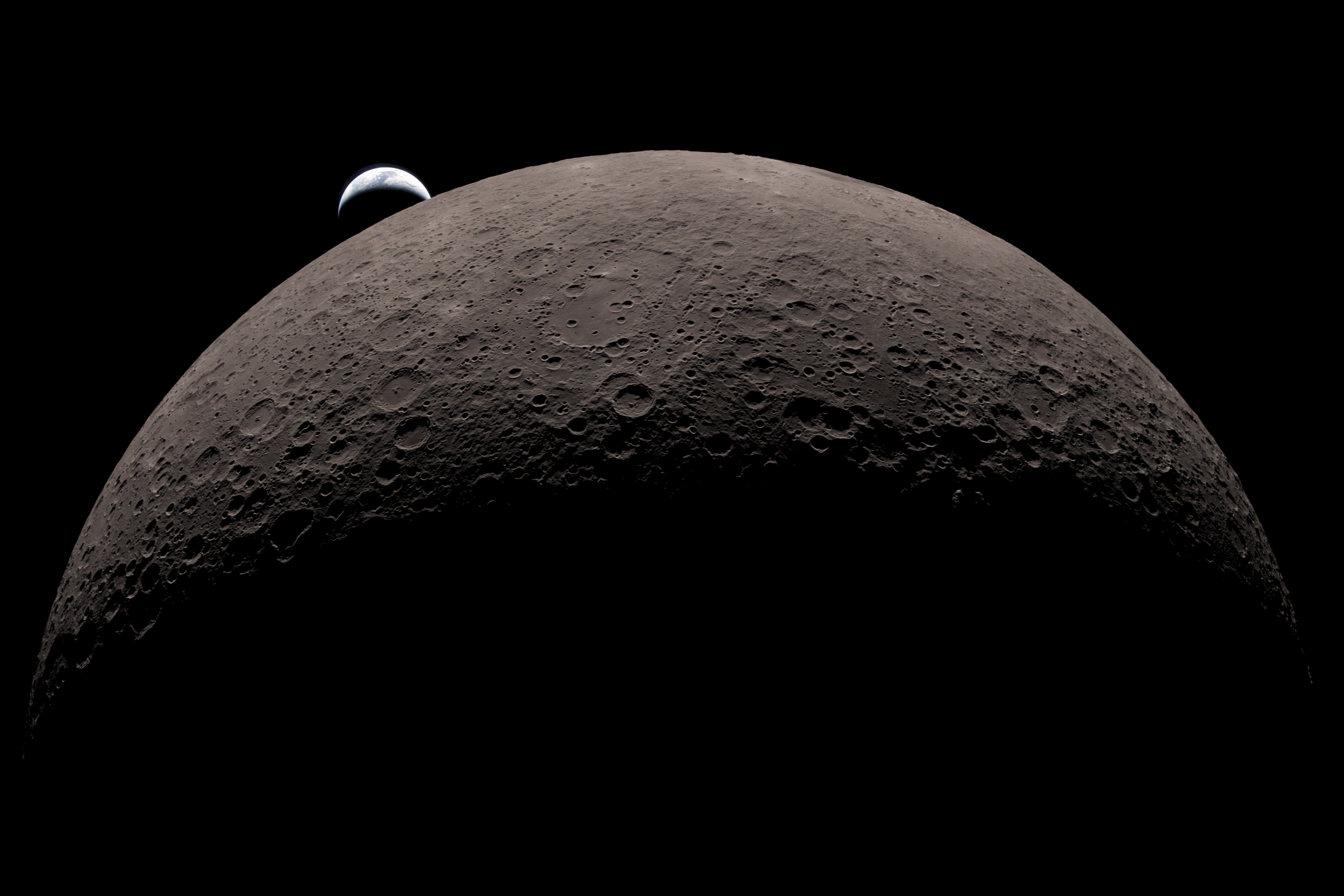 The Moon's cratered surface lit from below with Earth rising behind the horizon