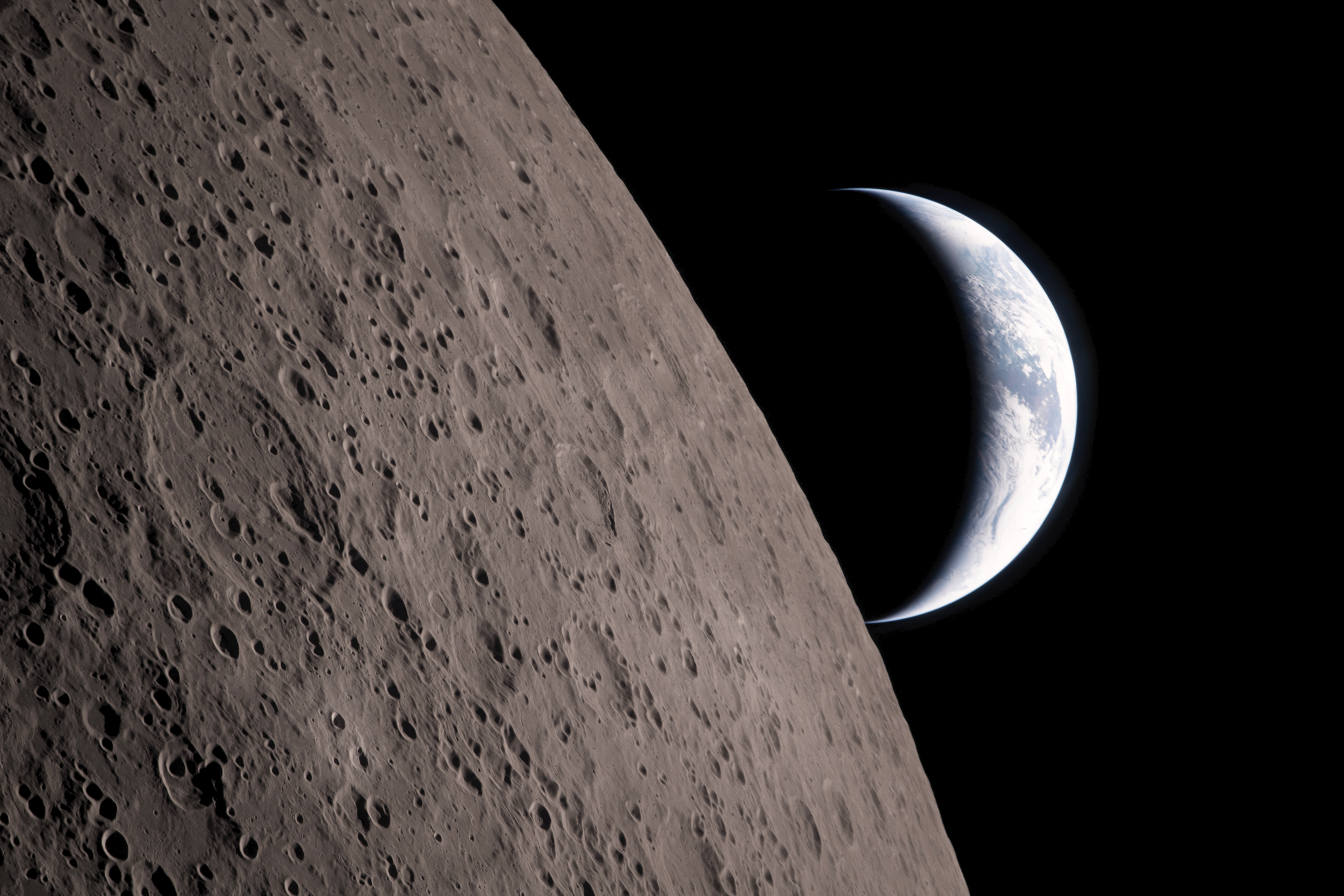 Close-up of the Moon's cratered terrain with Earth peeking over the top of the horizon